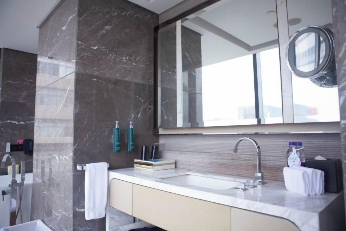 A modern bathroom with a marble sink, a large mirror, and toiletries on the wall.