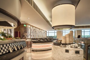 A modern hotel lobby with a central reception desk, a large window offering a view, and a decorative wall with a geometric pattern.