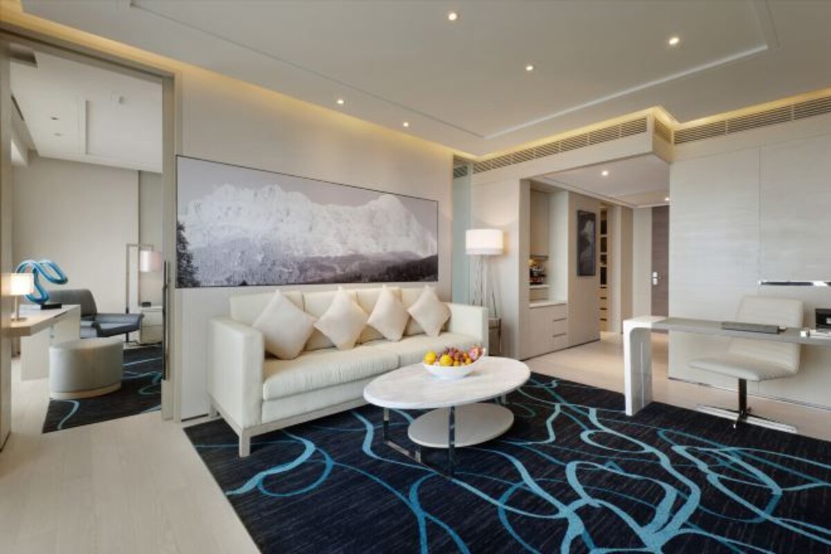A modern hotel room with a white sofa, a round coffee table, and a large abstract painting on the wall.