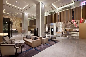 A spacious lobby with a reception desk, seating area, and a modern design with a large column and decorative elements.