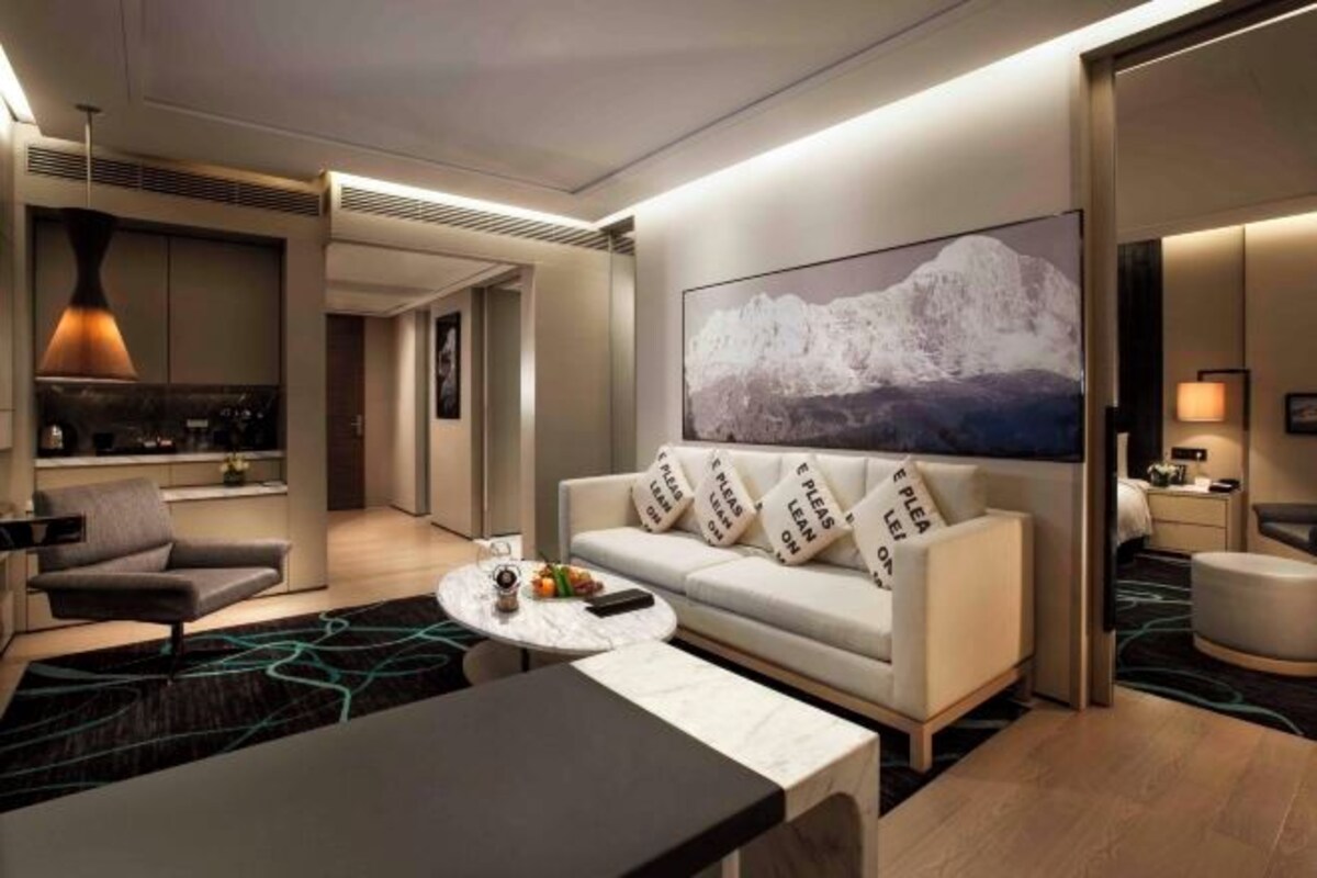 A modern hotel room with a sofa, a dining table, and a large painting of a mountain.