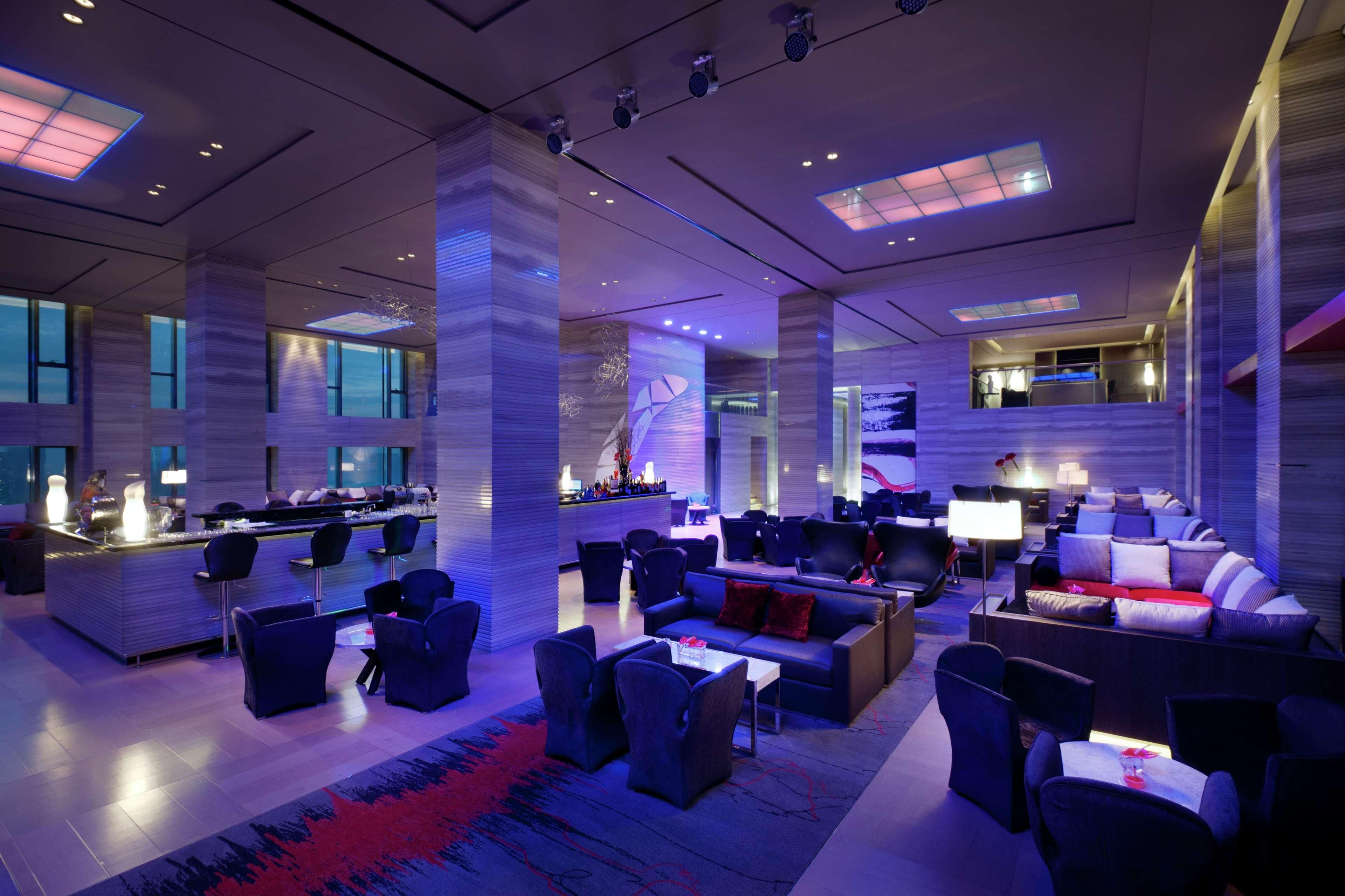 A modern hotel lobby with a bar area, seating arrangements, and large windows.