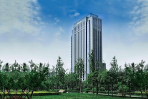 A tall, modern hotel building with a glass facade, surrounded by a well-maintained park with trees and a lawn. - Hilton Xi'an High-tech Zone (Xi'an)