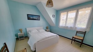 A bedroom with a bed, a chair, a nightstand, a lamp, a picture on the wall, and a window with curtains.
