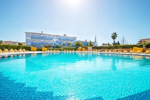 A swimming pool with lounge chairs, a building with balconies, and a clear sky.