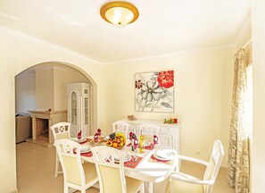A dining area with a white table set for four, a white cabinet with a decorative item on top, and a large floral painting on the wall. - Townhouse pool and jacuzzi in Portimão (Portimão)