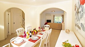 A dining area with a long table set for four, white chairs, a fruit basket, wine bottles, and a red centerpiece. - Townhouse pool and jacuzzi in Portimão (Portimão)