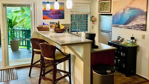 A kitchen with a central island, bar stools, a refrigerator, and a window with blinds.