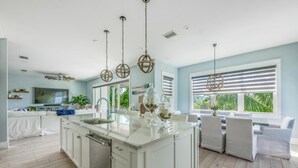Una cocina amplia con una isla central, armarios blancos y un ventanal con persianas.