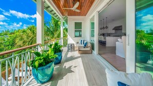 Un balcón amplio con piso de madera, plantas en macetas y un área de descanso con sofá y sillones.