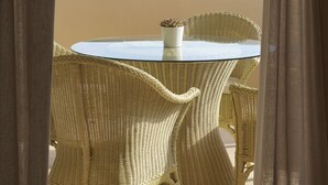 A wicker table and chairs under a pergola, overlooking a rocky landscape with vegetation and buildings. - One bed, fully detached apartment, 1 bath, sea view, communal pool, breakfast (Naxos)