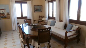 A dining area with a round table, chairs, a sofa, and a chandelier. - One bed, fully detached apartment, 1 bath, sea view, communal pool, breakfast (Naxos)