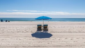 A beach with two blue chairs under a blue umbrella, a sandy beach, and the ocean in the background. - Boardwalk   983 (Gulf Shores)