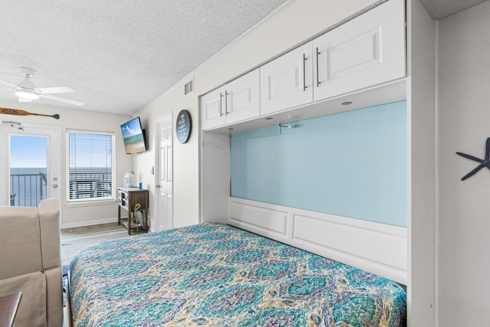A bedroom with a bed, a TV, a clock, and a window with a view.