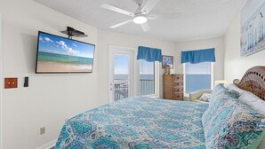 A bedroom with a large bed, a ceiling fan, a TV on the wall, and a view of the ocean through the window. - Boardwalk   983 (Gulf Shores)