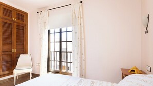 Ein Schlafzimmer mit einem Bett, einem Sessel, einem Fenster mit Vorhängen und einem Holzschrank.