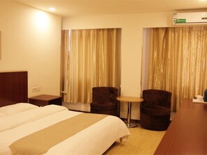 A hotel room with a bed, two armchairs, a small table, and a wooden desk.