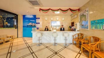 A hotel reception area with a marble counter, bar stools, and wicker chairs.