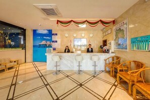 A hotel reception area with a marble counter, bar stools, and wicker chairs. - GreenTree Alliance Hotel (Xiamen Railway Station Sports Center) (Xiamen)