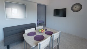A modern dining area with a wooden table, purple placemats, and a fruit bowl. - Paulsia Apartments (Rhodes)