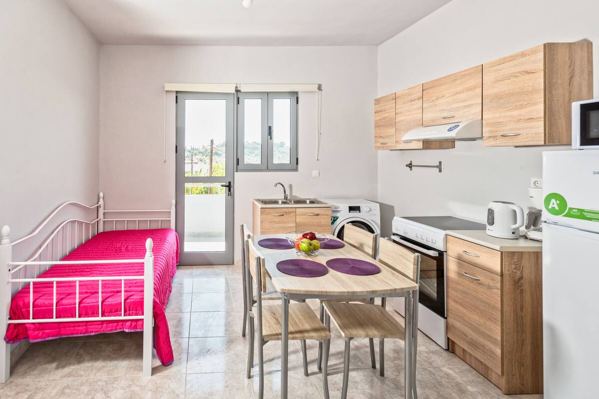 A compact kitchen with a bed, a dining table, and a window.