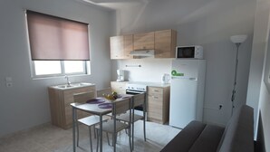 A compact kitchen with a dining table, chairs, a microwave, a coffee maker, and a refrigerator. - Paulsia Apartments (Rhodes)