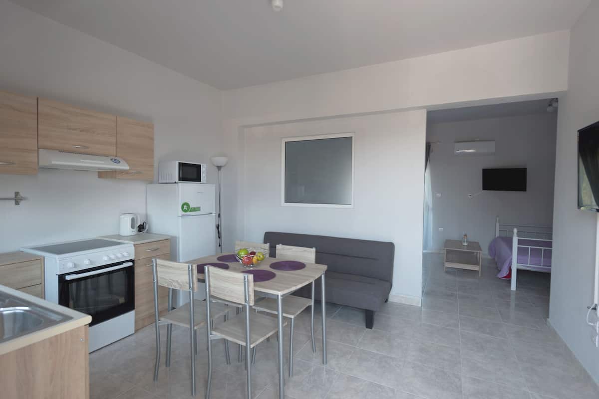 A modern kitchen with a stove, microwave, and refrigerator. There is a dining table with chairs and a gray sofa in the living area.