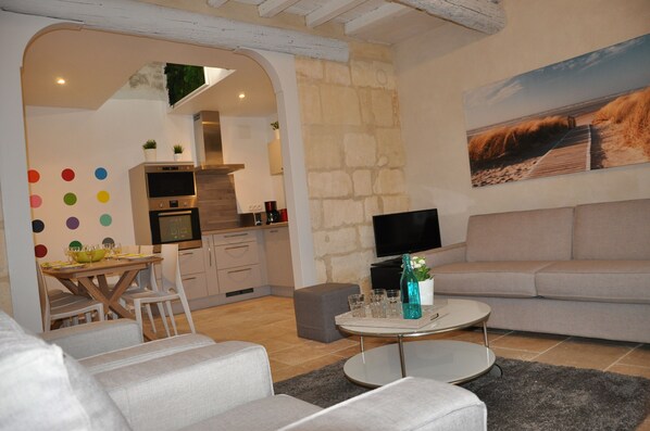 A modern living room with a grey sofa, a round coffee table, and a dining area with a wooden table and chairs.