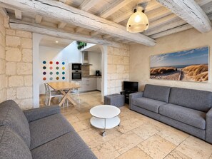 A modern living room with a grey sofa, a round coffee table, and a dining area with a wooden table and chairs.