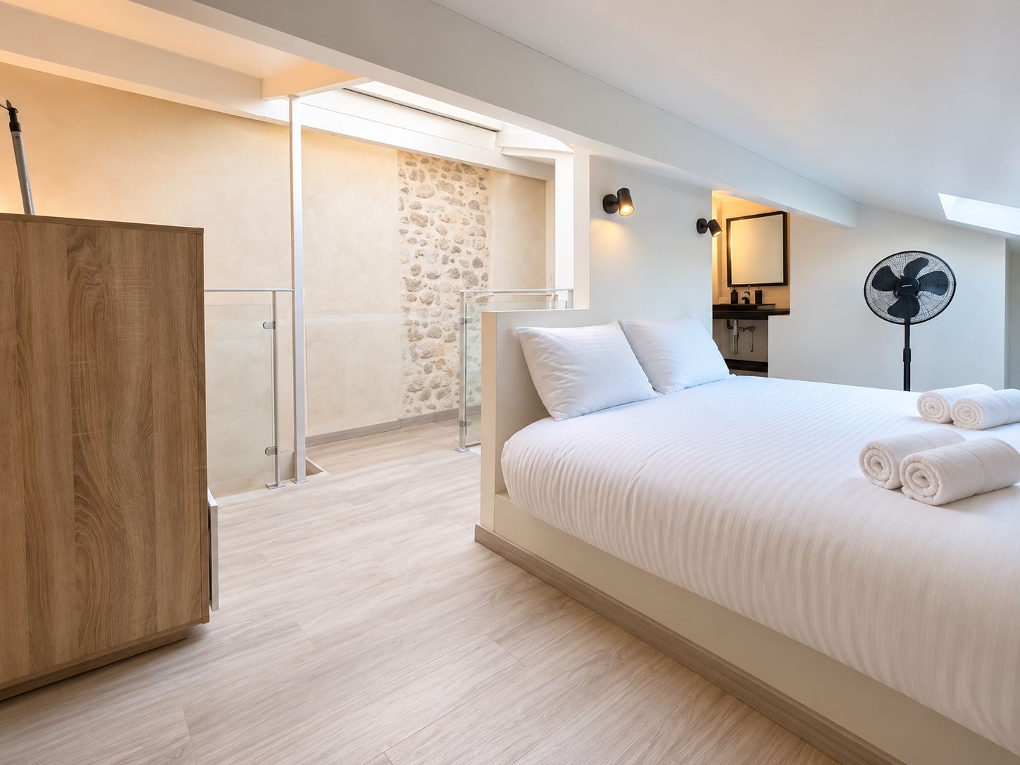 Quarto de hotel moderno com uma cama grande, um guarda-roupa de madeira, uma parede de pedra e uma varanda com porta de vidro.