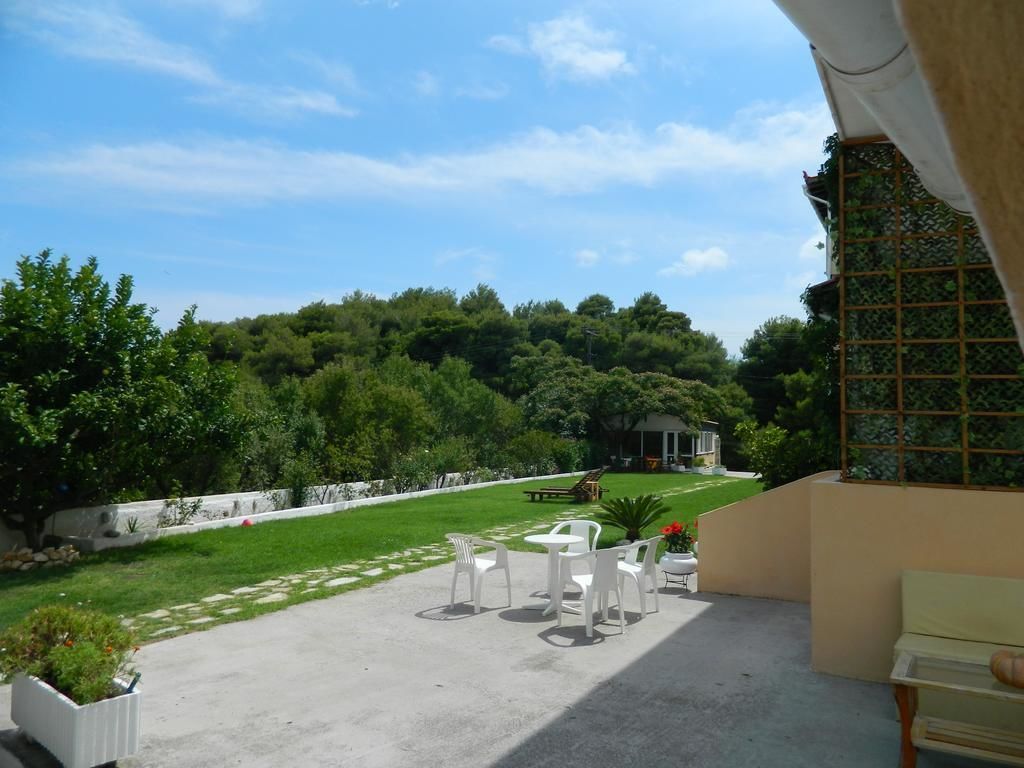 Un patio con sillas y una mesa de plástico blanco, con vista a un césped cuidado y una casa al fondo.