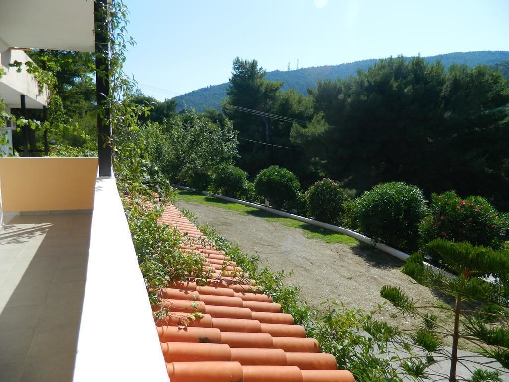Un balcón con baldosas de terracota, vistas a un jardín ajardinado y una cadena montañosa distante.