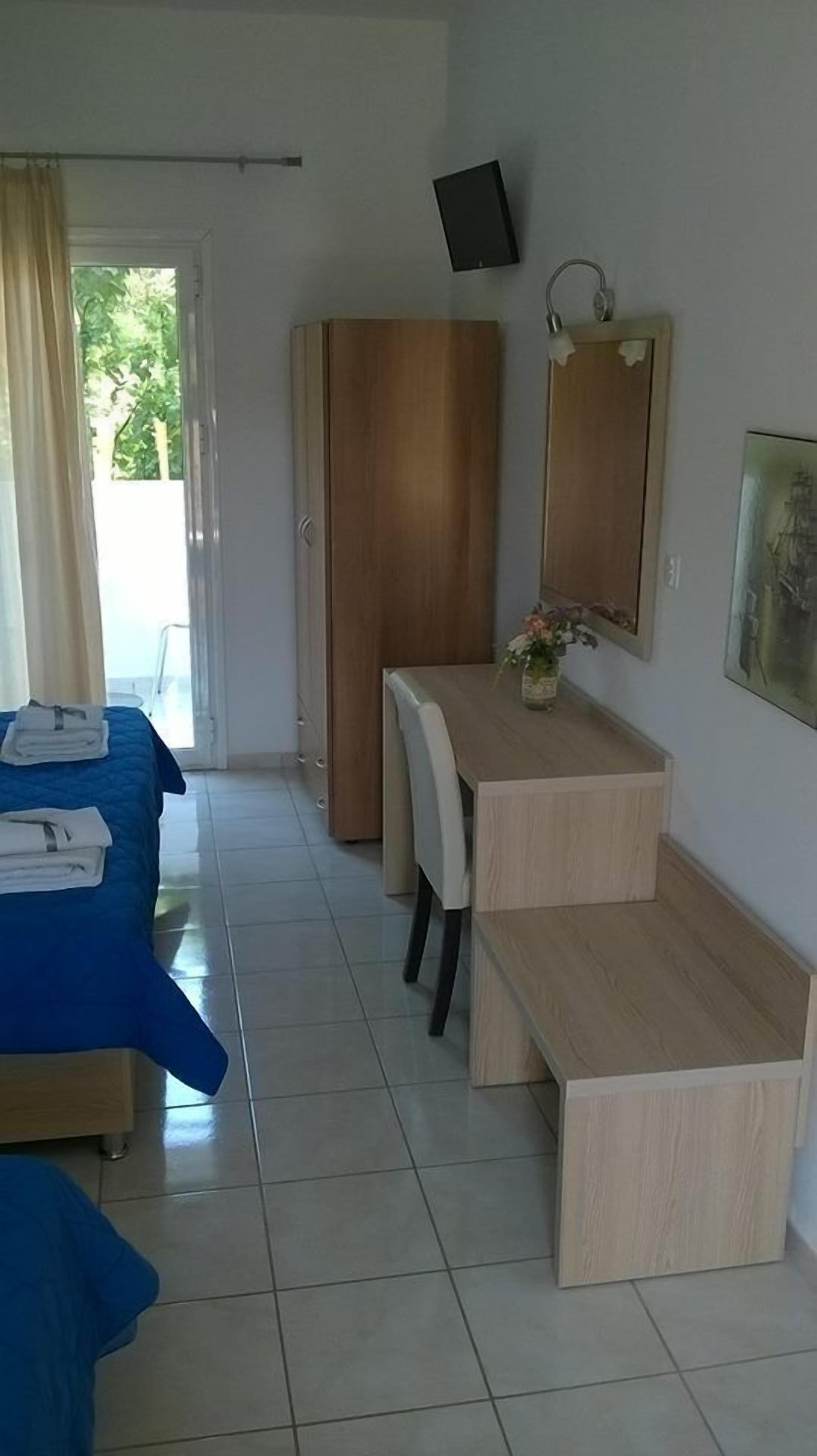 Habitación de hotel con una cama, un escritorio con silla, una mesita, un espejo y un televisor en la pared.