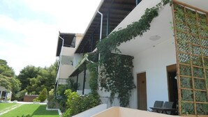 A modern two-story building with a flat roof, a balcony with a wooden trellis, and a garden area with a lawn and potted plants. - Asteri Studio's (Skiathos)