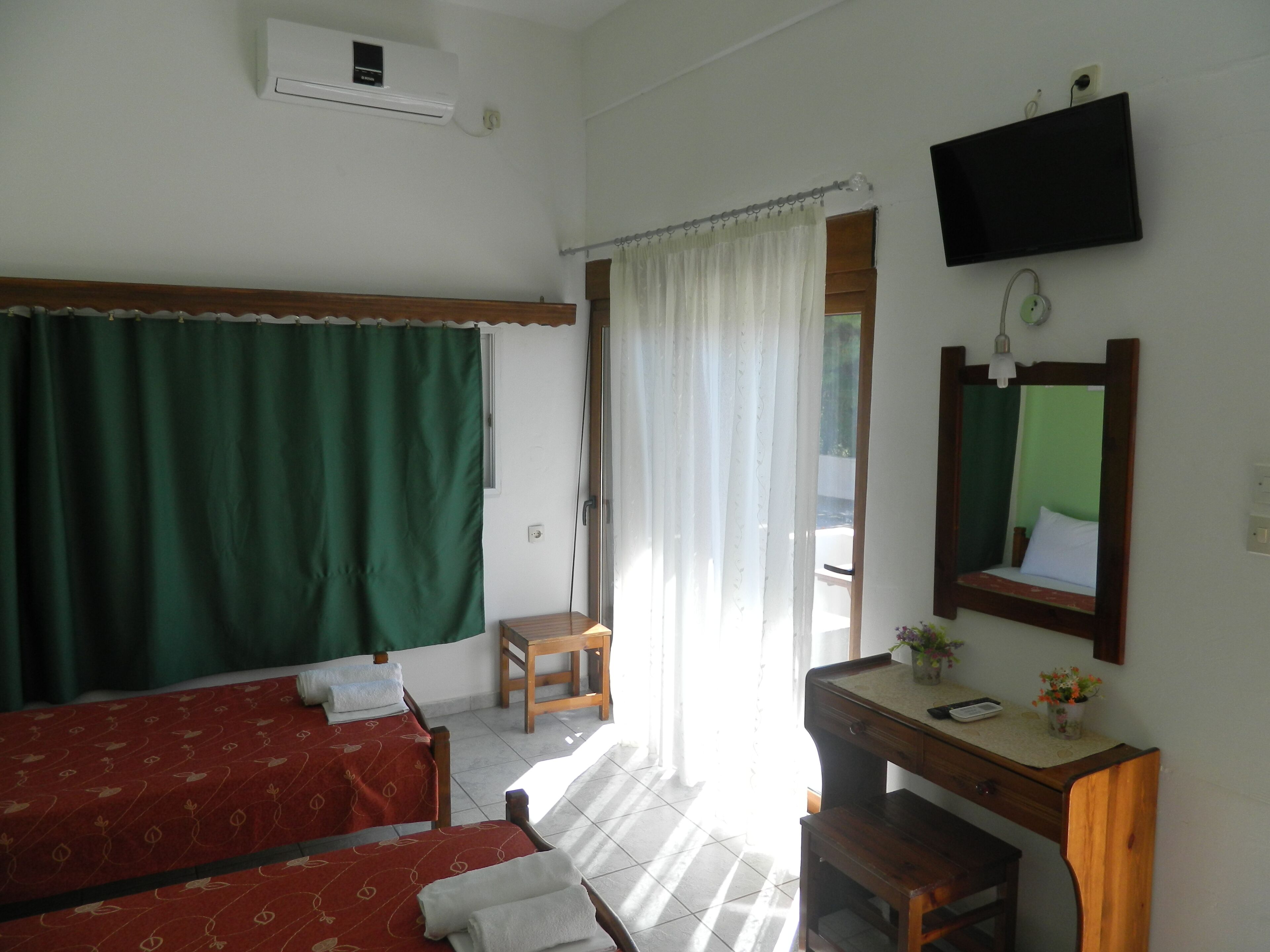 Una habitación con dos camas, un escritorio, una silla, un televisor y una ventana con cortinas.