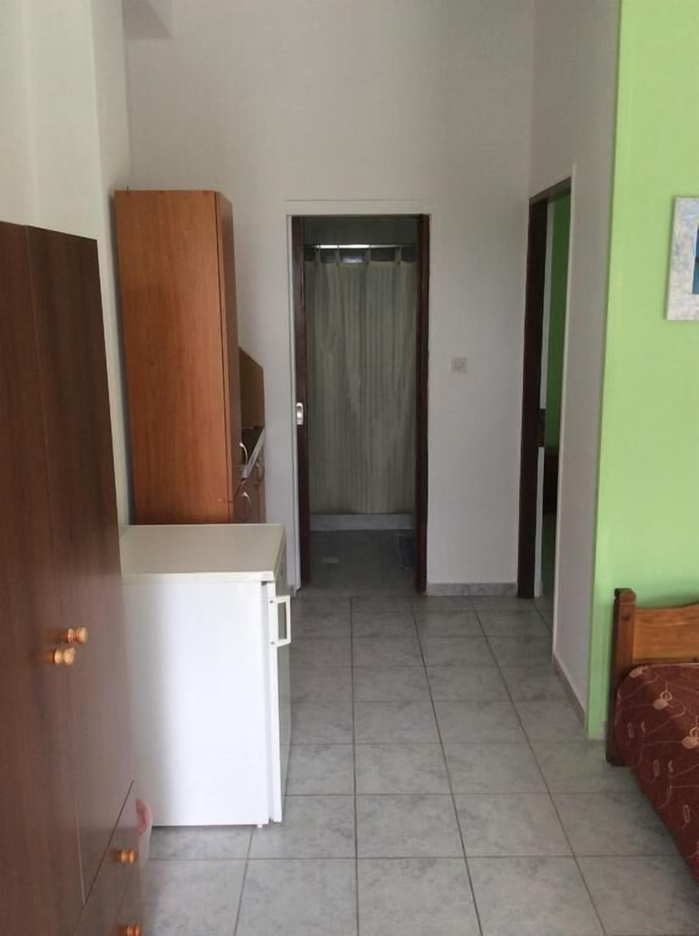 A narrow hallway with a wooden wardrobe, a white cabinet, and a green wall.