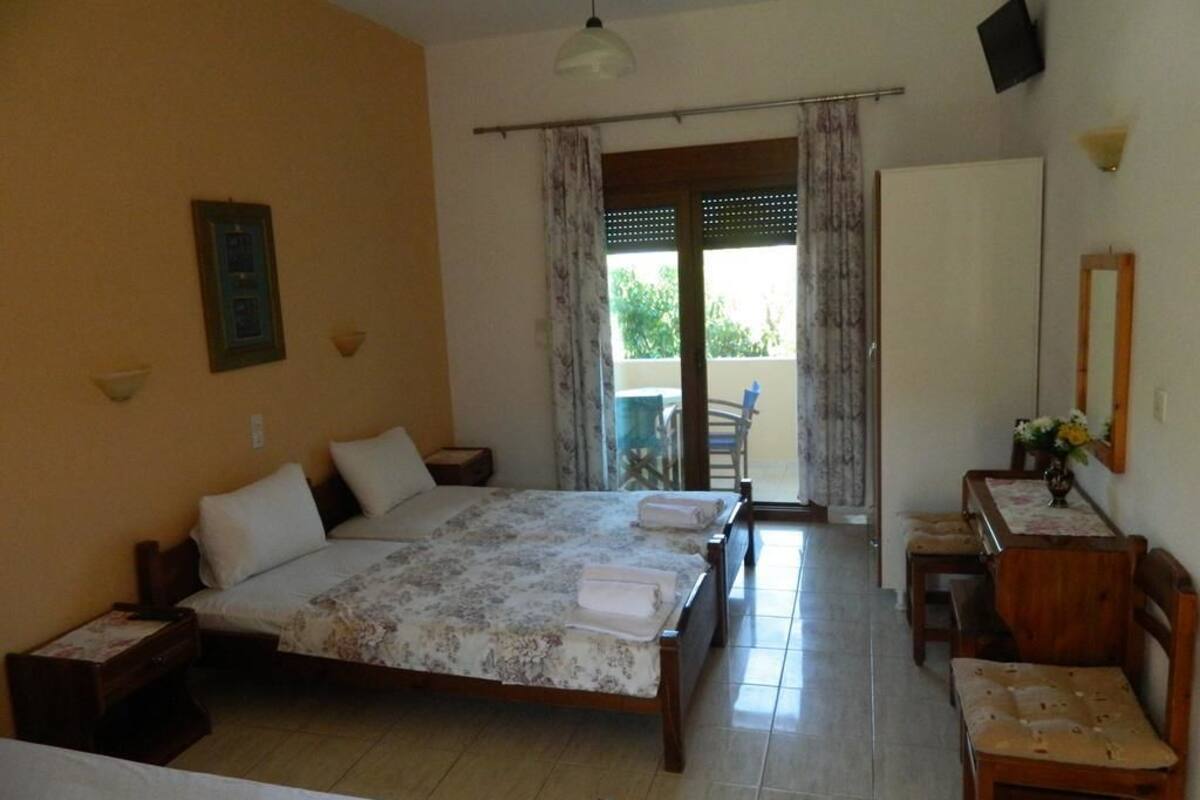 A hotel room with a bed, bedside tables, a desk, and a chair. There is a balcony with a view of greenery.