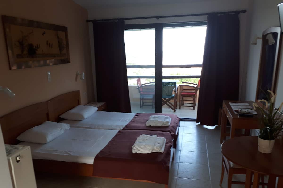 A hotel room with two beds, a desk, and a balcony with chairs.
