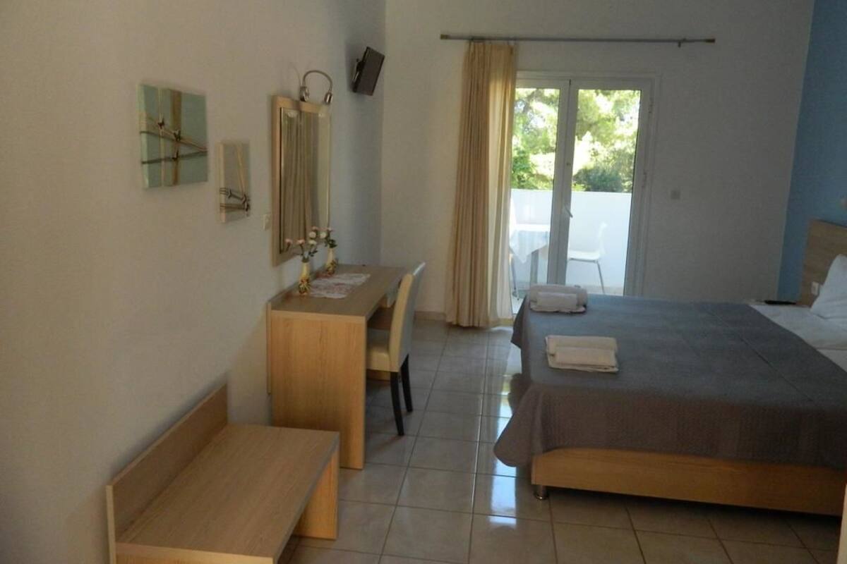 A hotel room with a bed, a desk, a chair, a mirror, and a view of the outdoors.