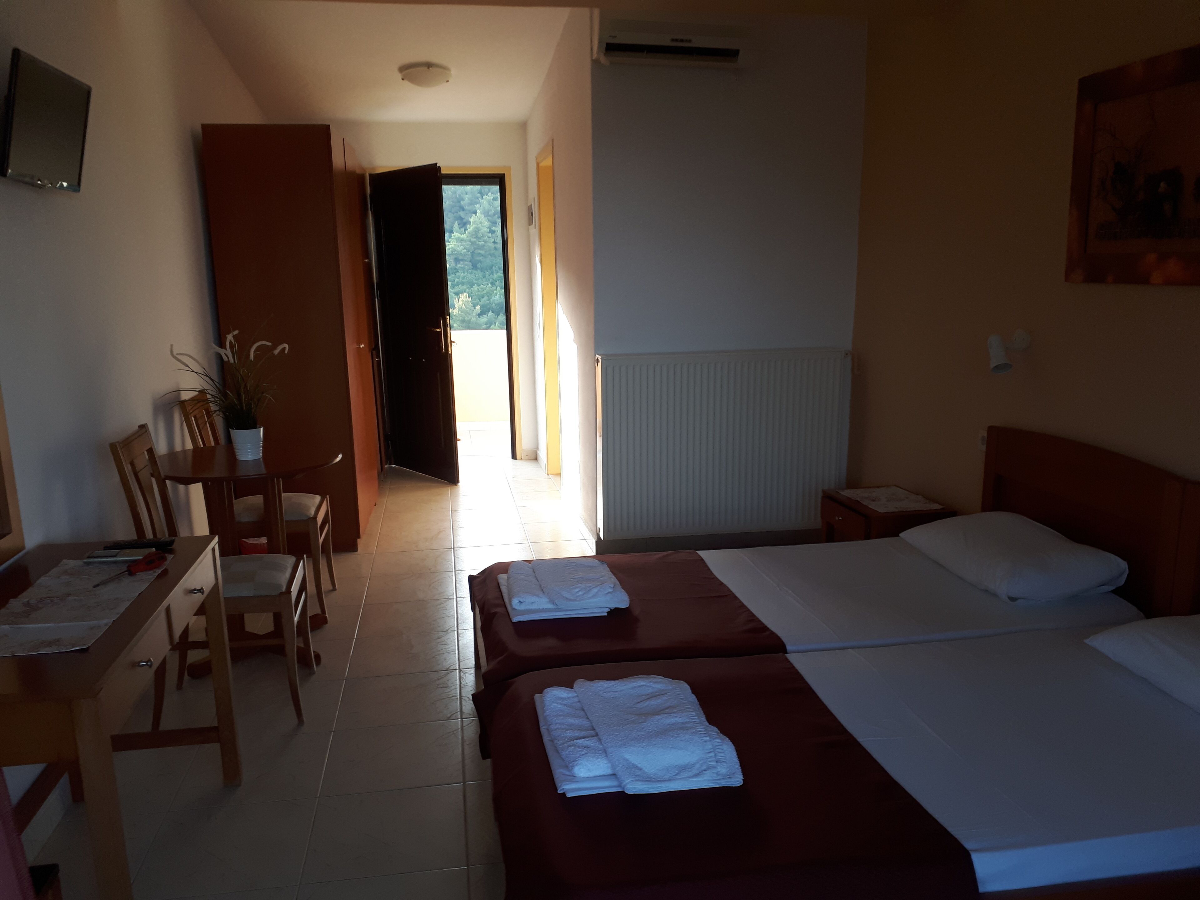Een hotelkamer met twee bedden, een bureau met stoel, een potplant en uitzicht op het omliggende landschap.