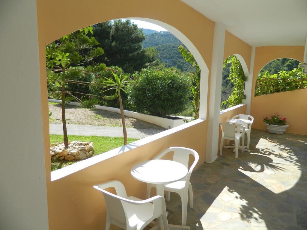 Un espacio de estar al aire libre techado, con sillas y mesas blancas, que ofrece vistas a un jardín ajardinado y un paisaje montañoso.