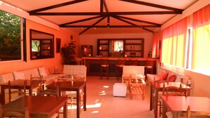 A spacious living area with a high ceiling and exposed beams, a kitchen area with bar seating, and a dining area with multiple tables and chairs. - Asteri Studio's (Skiathos)