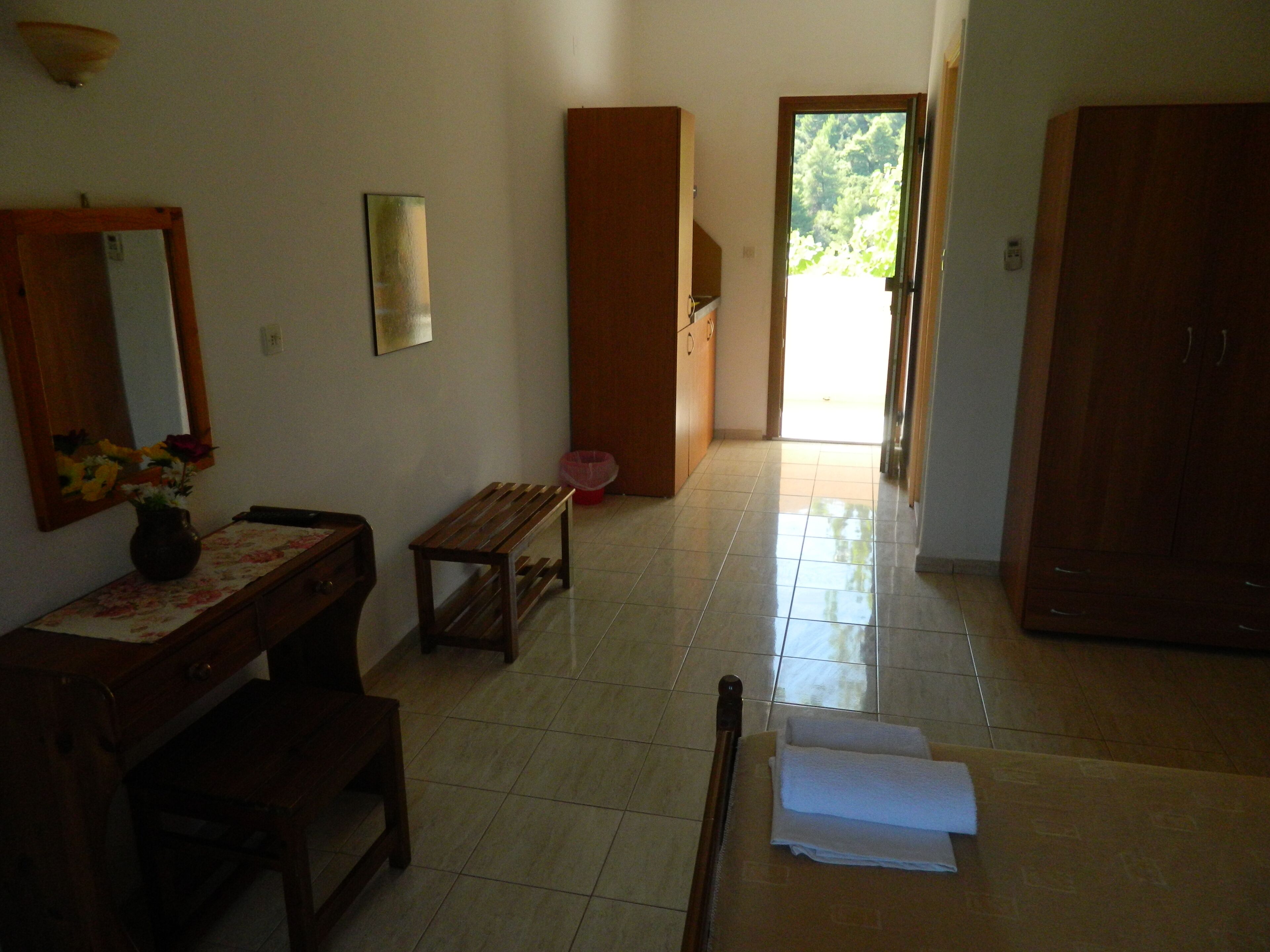 A room with a wooden desk, a bench, a mirror, and a door leading to a bright outdoor area.