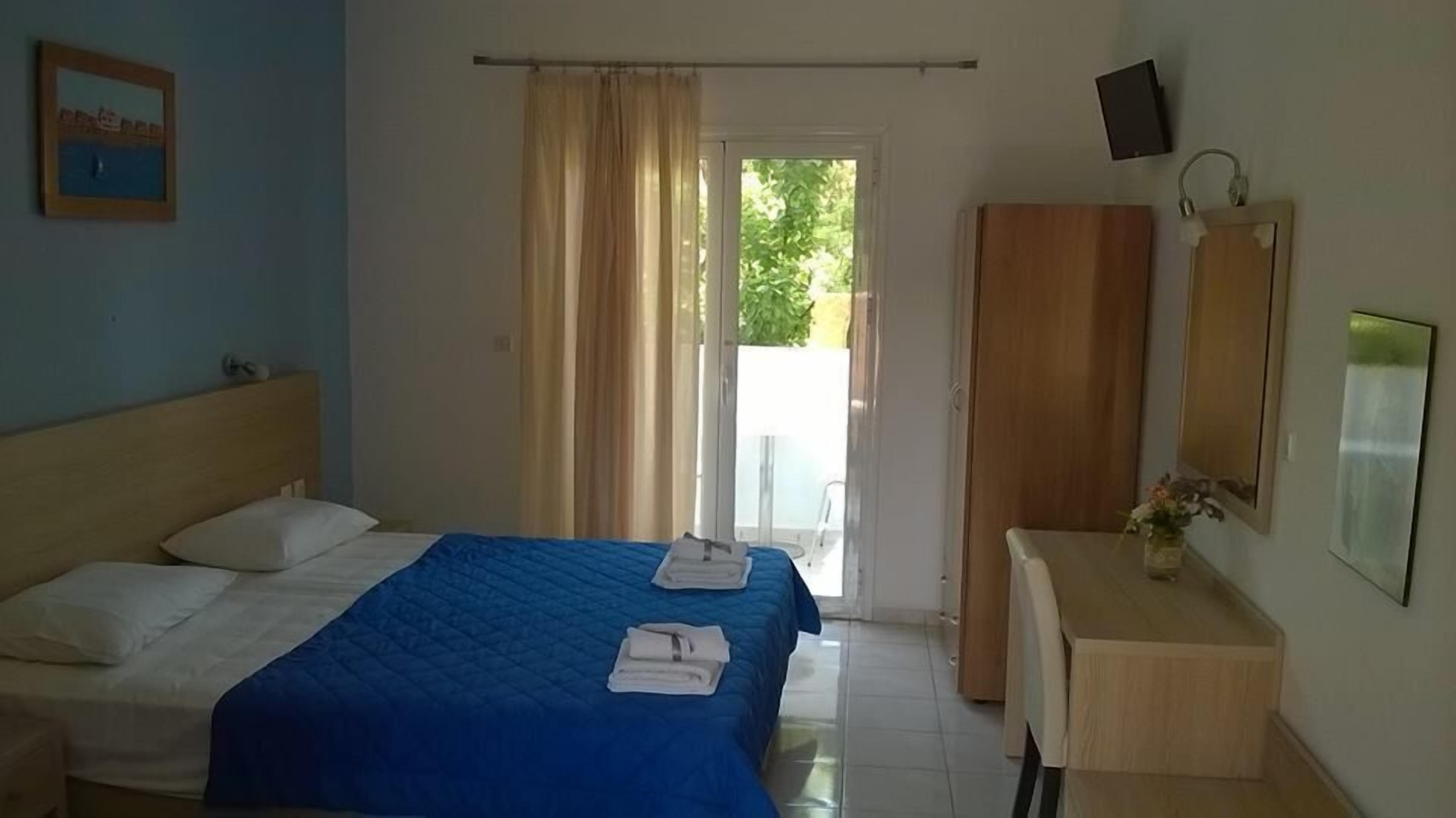 A hotel room with a bed, a desk, a mirror, and a window with curtains.