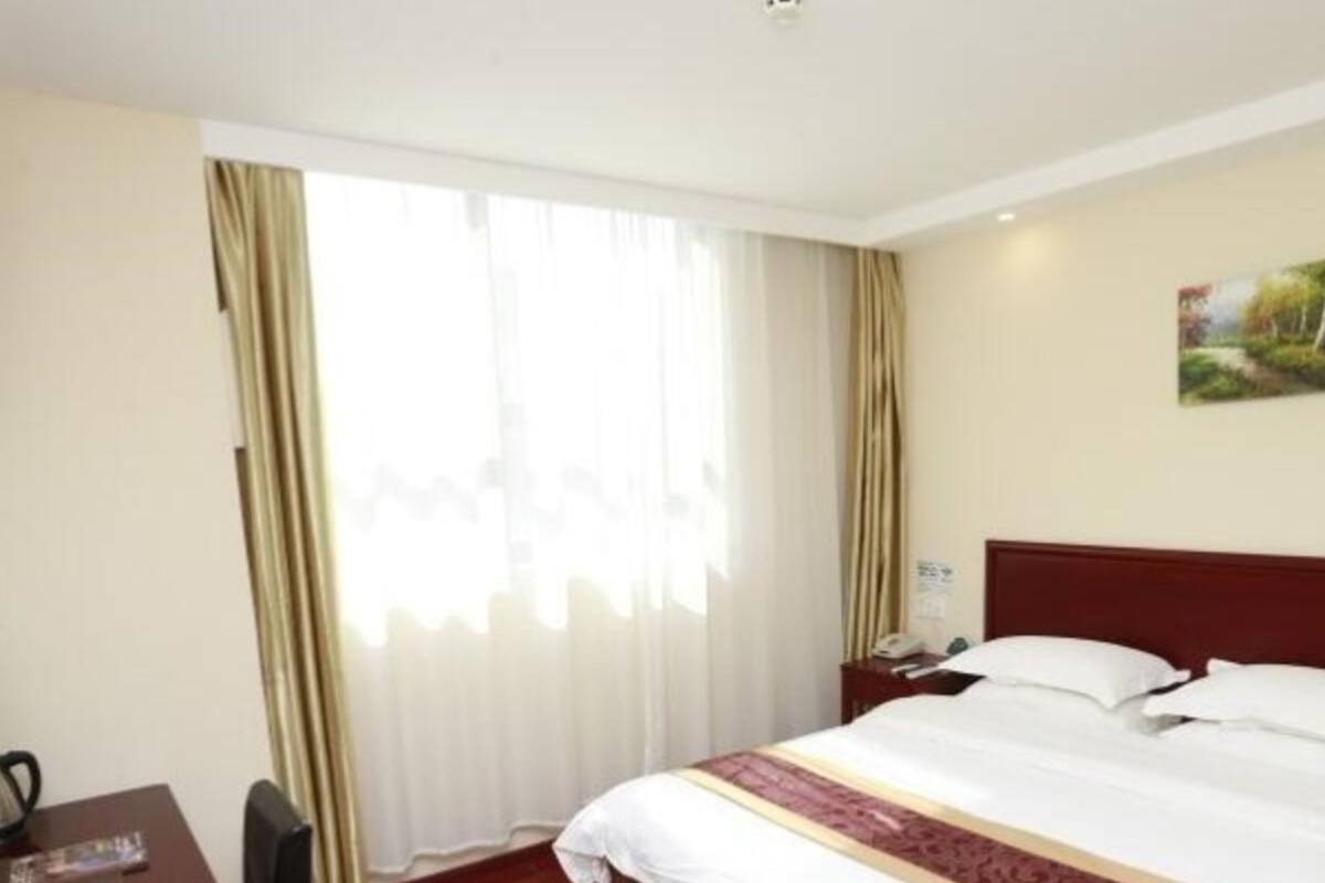 A hotel room with a bed, a desk, a chair, and a painting on the wall.