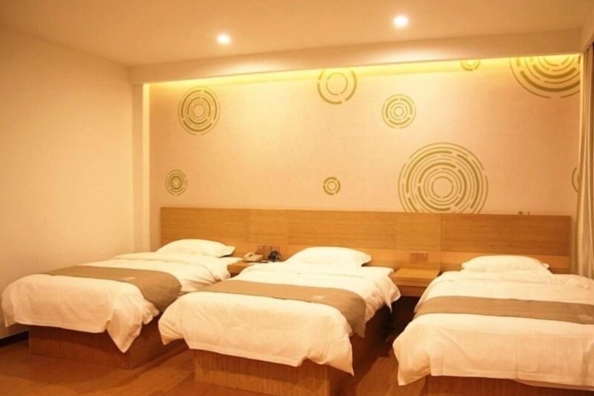 Habitación de hotel con cuatro camas individuales, cabecero de madera y pared con diseños circulares.