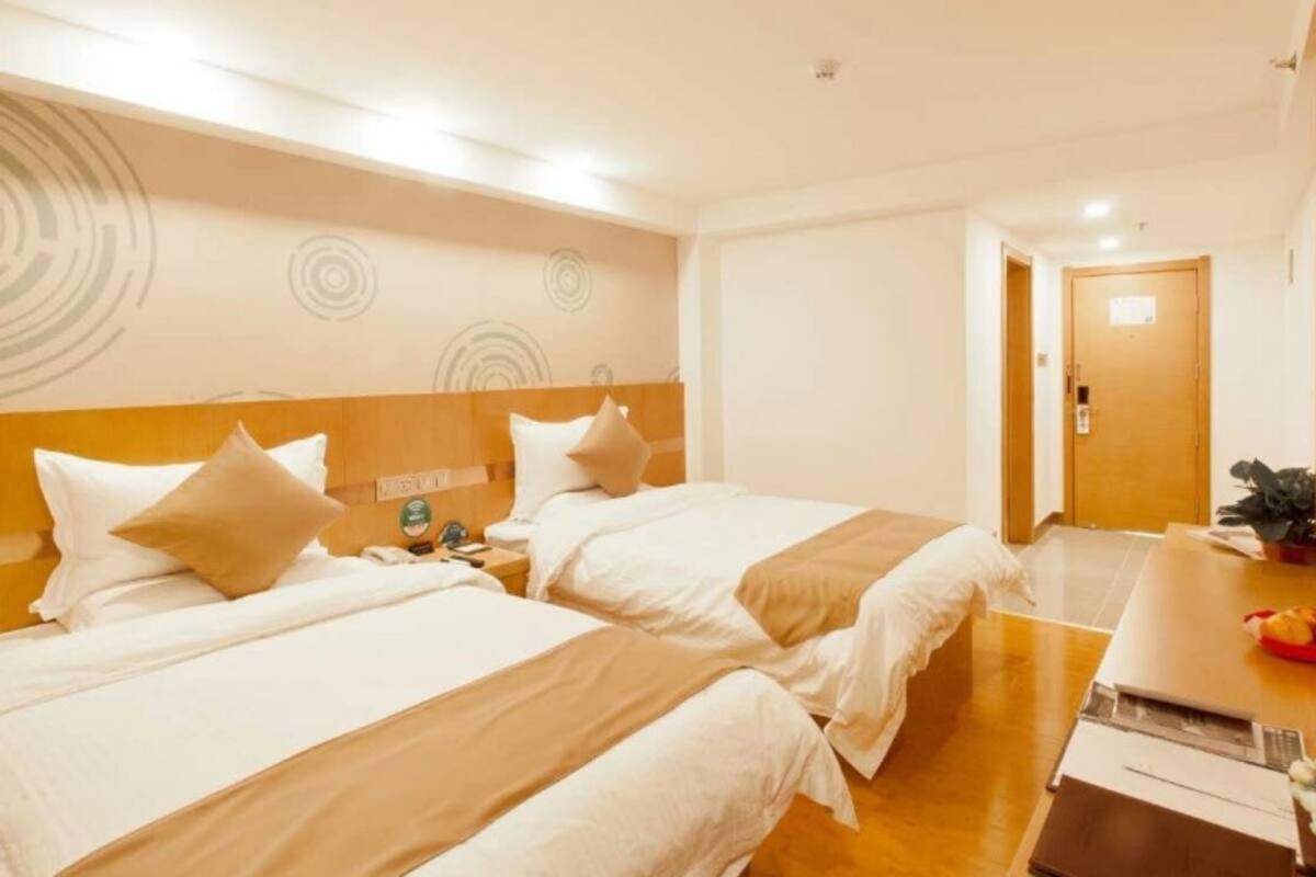 Habitación de hotel con dos camas, un cabecero de madera, un escritorio con una computadora portátil y una puerta al fondo.