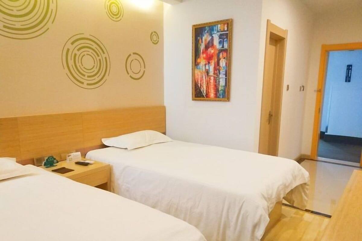 Habitación de hotel con dos camas, cabecero de madera, mesita de noche, un cuadro en la pared y una puerta que da a otra habitación.