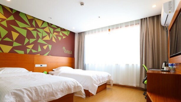 A hotel room with two beds, a wooden headboard, a geometric wall mural, a large window with curtains, and a desk with a mirror and a coffee maker. - Vatica Shanghai Jinshan District Jinshan Guojishangmaocheng Weihong Road Hotel (Shanghai)