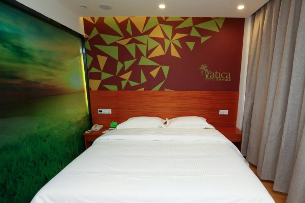 Une chambre d’hôtel avec un lit, une table de chevet, un téléphone et un mur orné de motifs géométriques.
